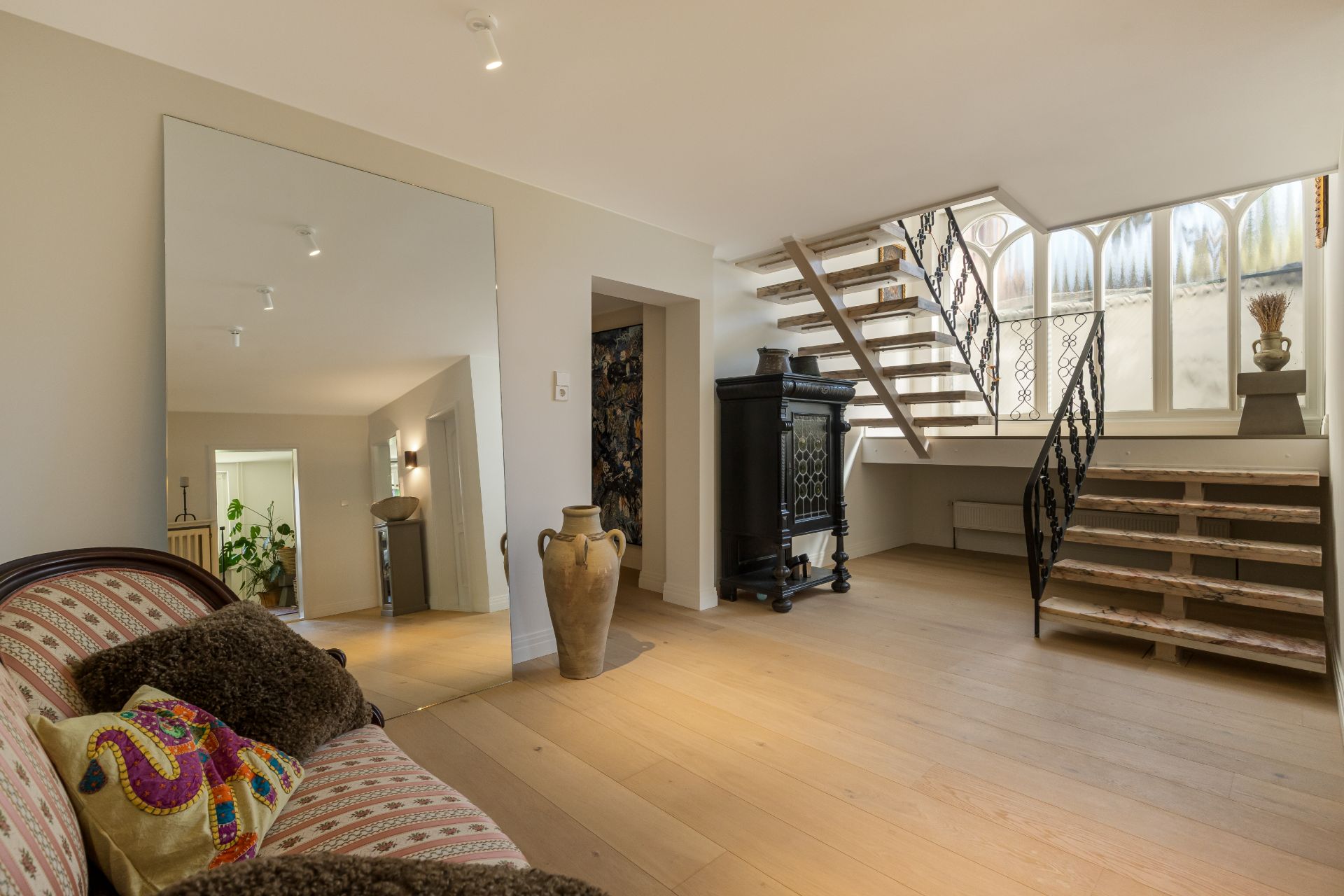 Heller Raum mit Holztreppe, großem Spiegel, Sofa, Vase und Schrank.