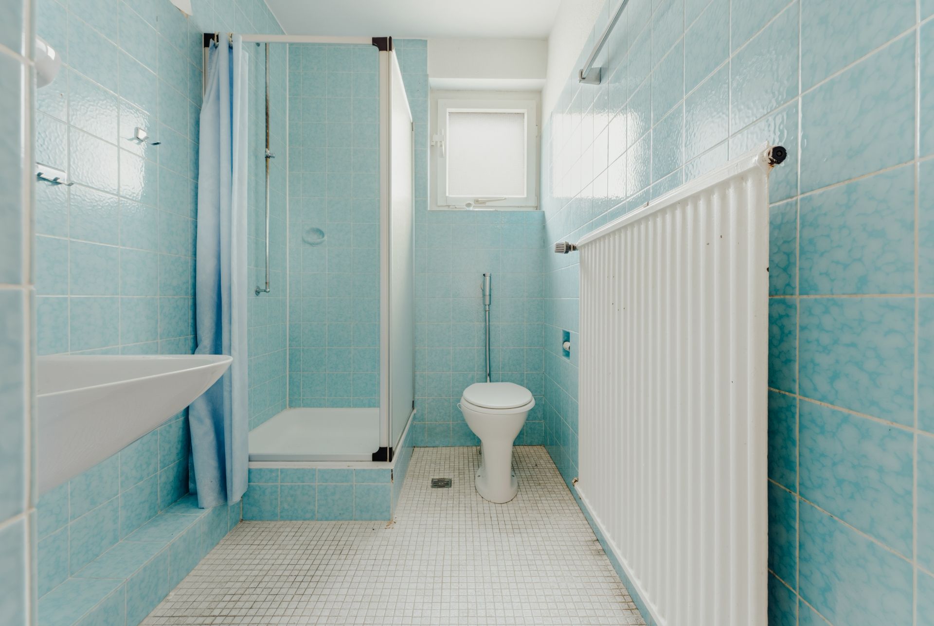Helles Badezimmer mit blauen Fliesen, Dusche, WC, Waschbecken und Fenster.