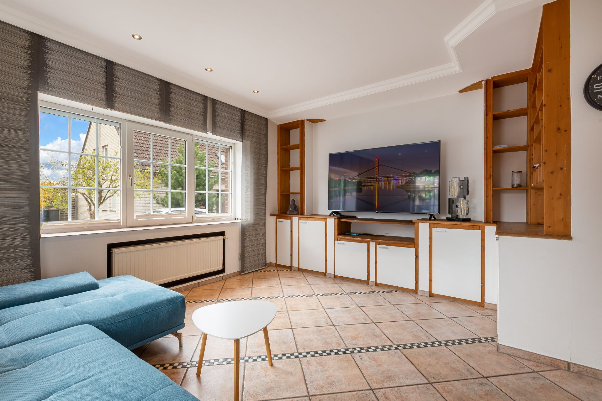 Wohnzimmer mit Ecksofa, Couchtisch, großem Fenster und Fernseher auf Schrankwand.
