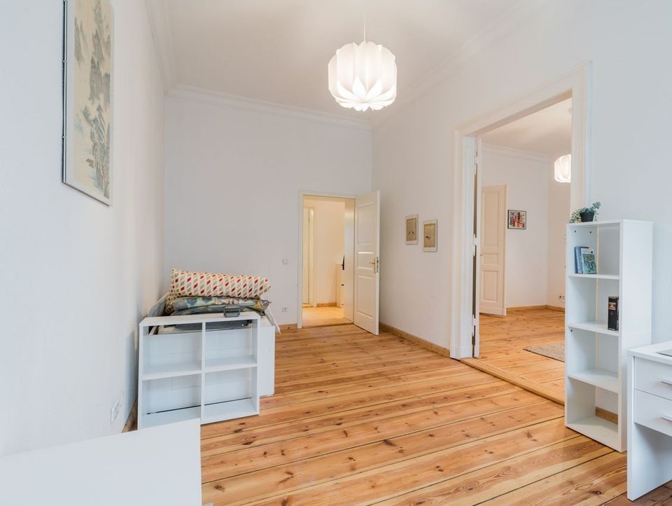 Helles Zimmer mit Holzboden, weißen Möbeln und offenen Türen zu weiteren Räumen.