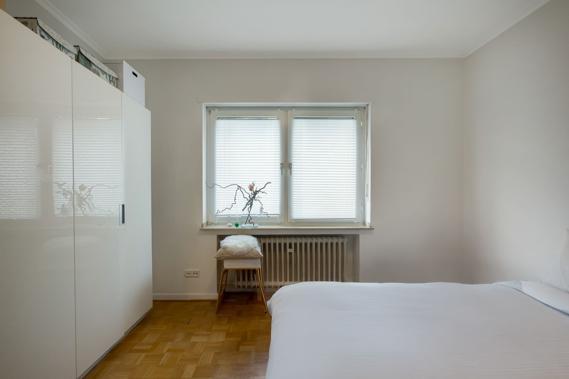 Schlafzimmer mit weißem Kleiderschrank, Doppelbett und Fenster mit Jalousien.