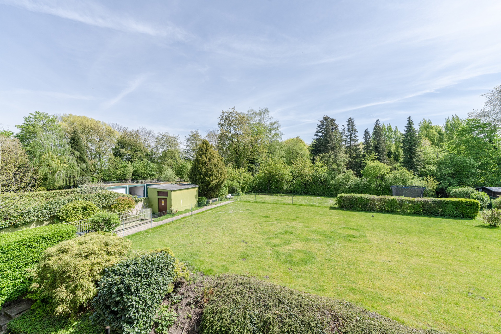 Großer, grüner Garten mit Rasen, Büschen, Bäumen und einem kleinen Schuppen am Rand.