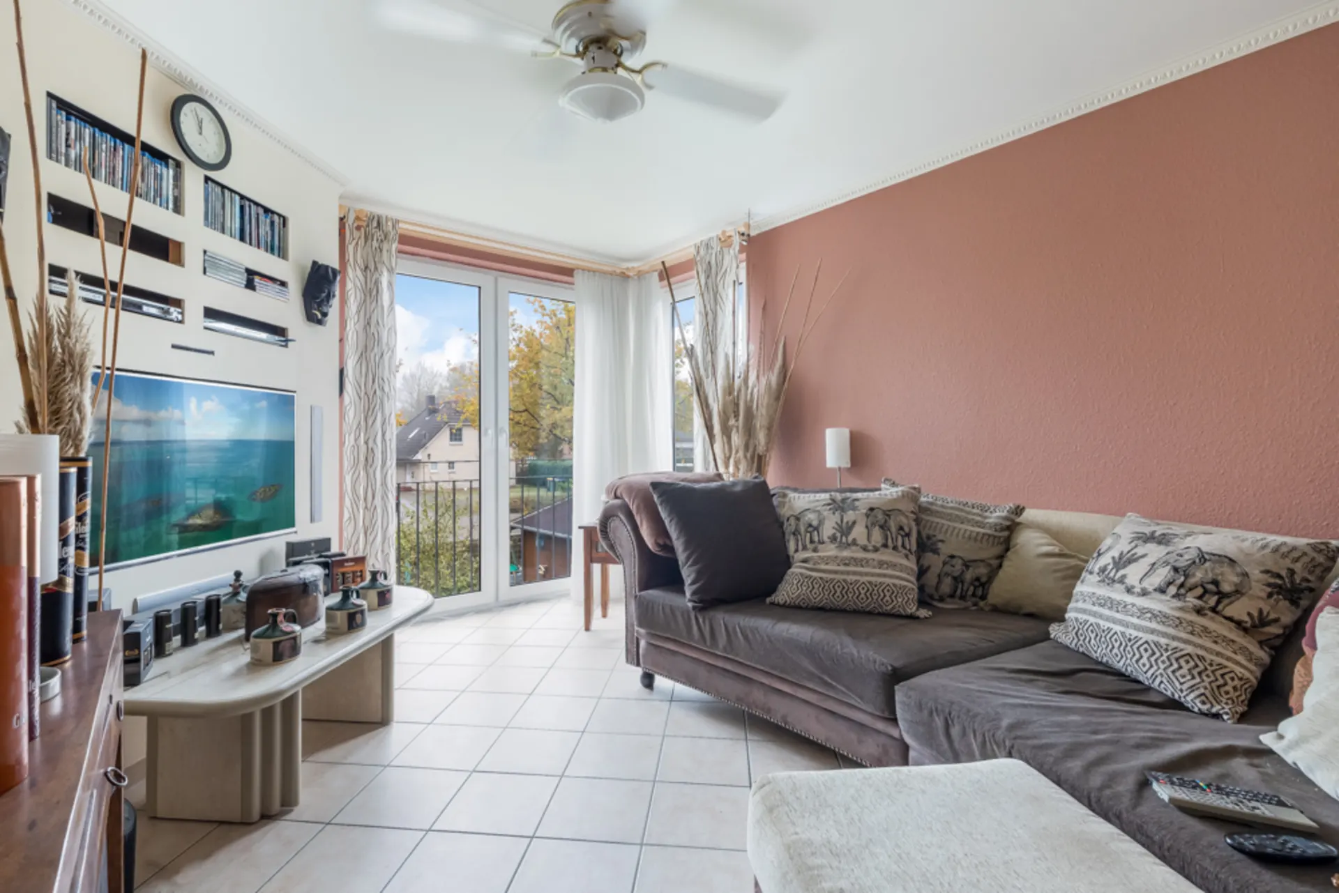 Helles Wohnzimmer mit Ecksofa, Kissen, Couchtisch und großen Fenstern mit Blick nach draußen.
