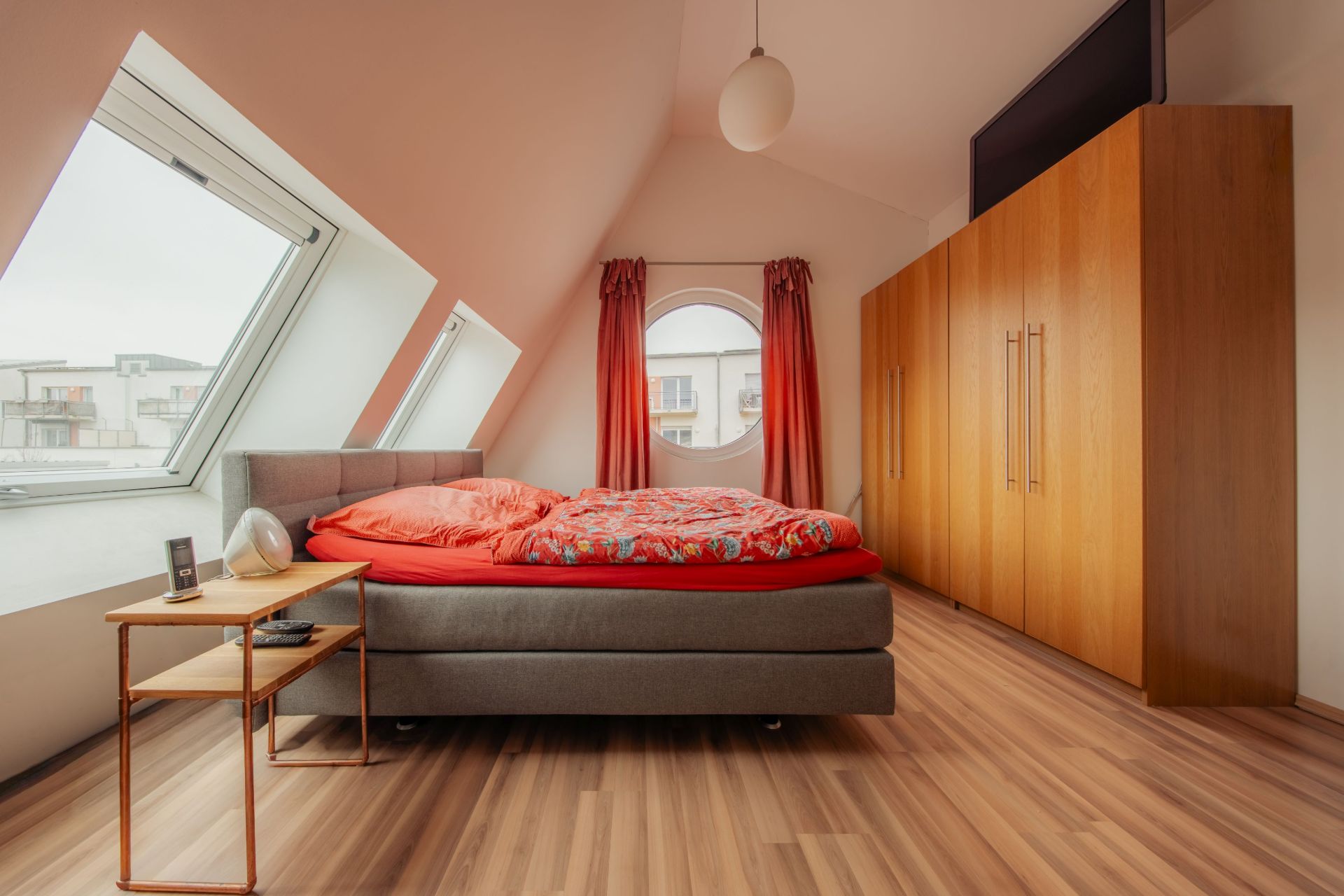Schlafzimmer mit Doppelbett, Holzschrank, Nachttisch und schrägen Fenstern auf Dachboden.