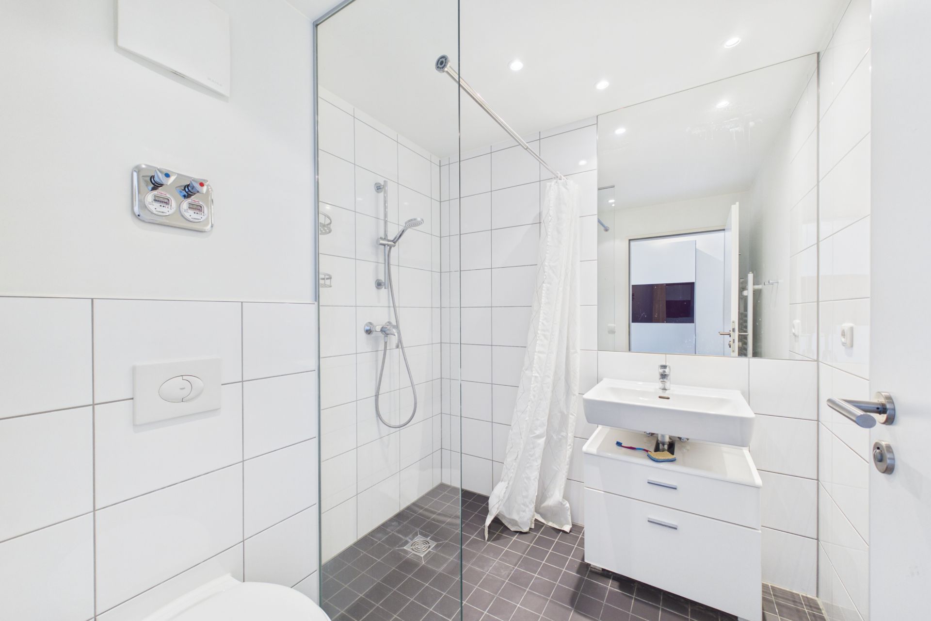 Modernes Bad mit Dusche, Waschbecken und Spiegel, weiße Fliesen und grauer Boden.