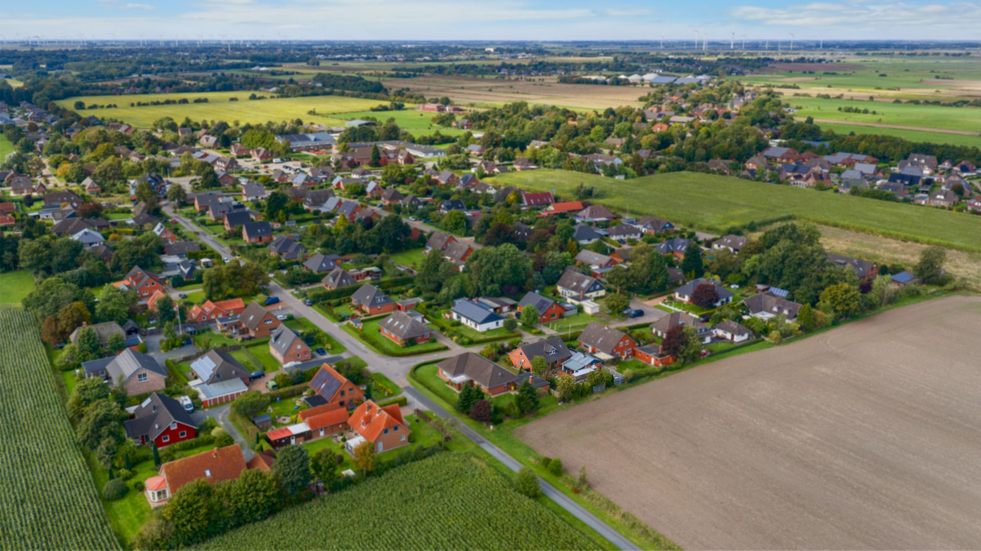 Luftaufnahme eines Wohngebiets mit Einfamilienhäusern neben Feldern und Straßen.