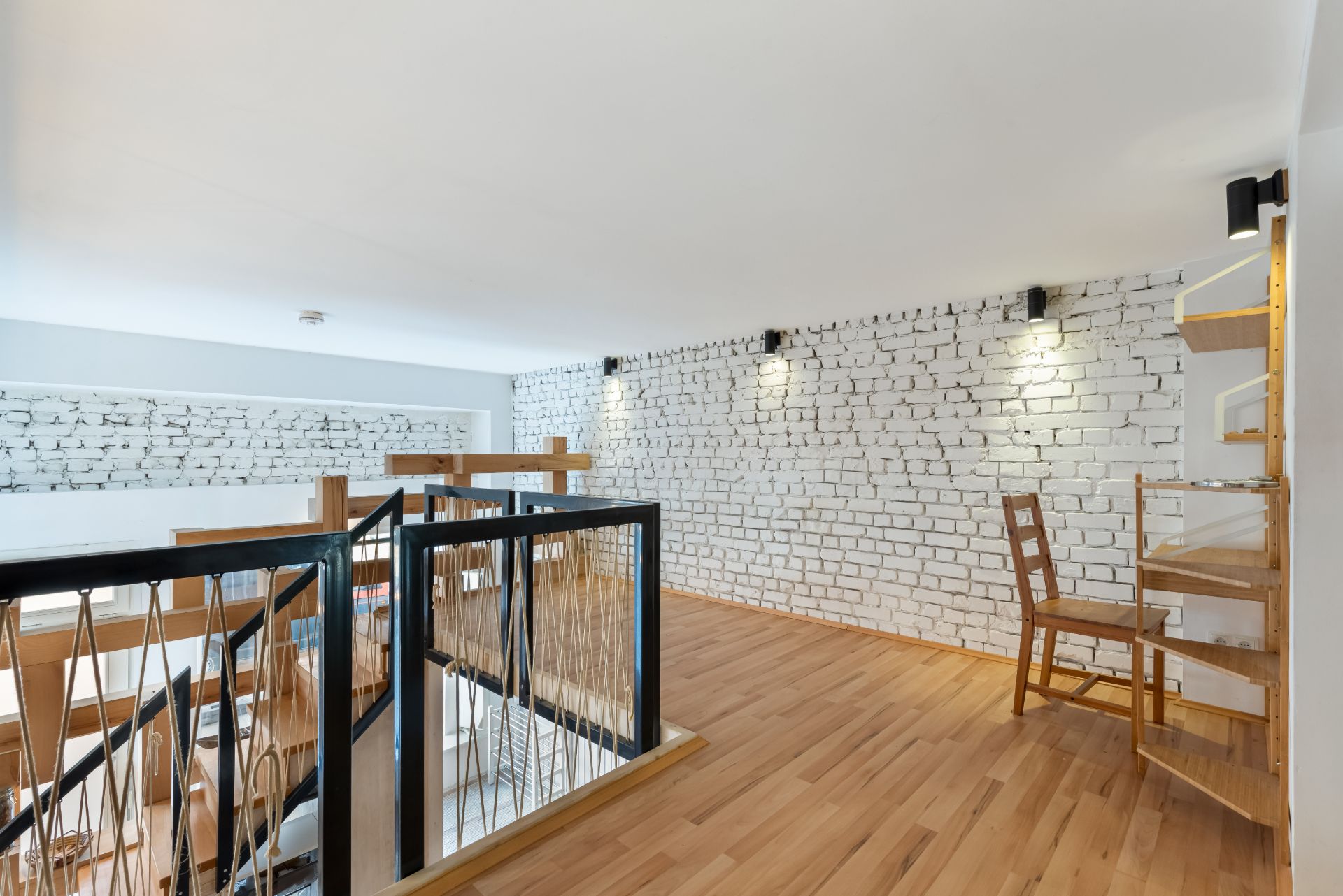 Heller Wohnbereich mit Holzfußboden, weißen Backsteinwänden und einem kleinen Schreibtisch mit Stuhl.