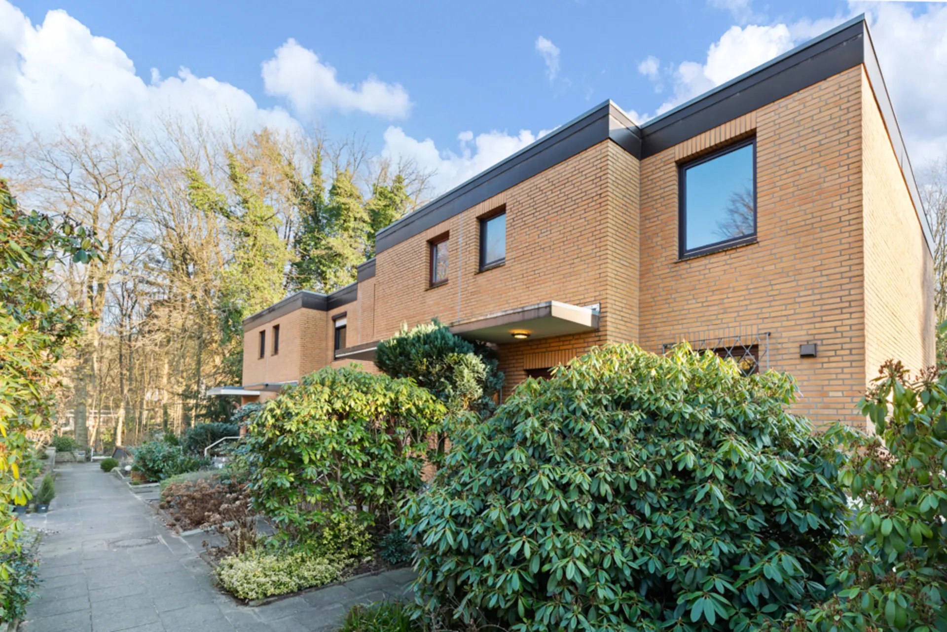 Modernes Wohngebäude mit gelber Klinkerfassade und großen Fenstern, umgeben von viel Grün.