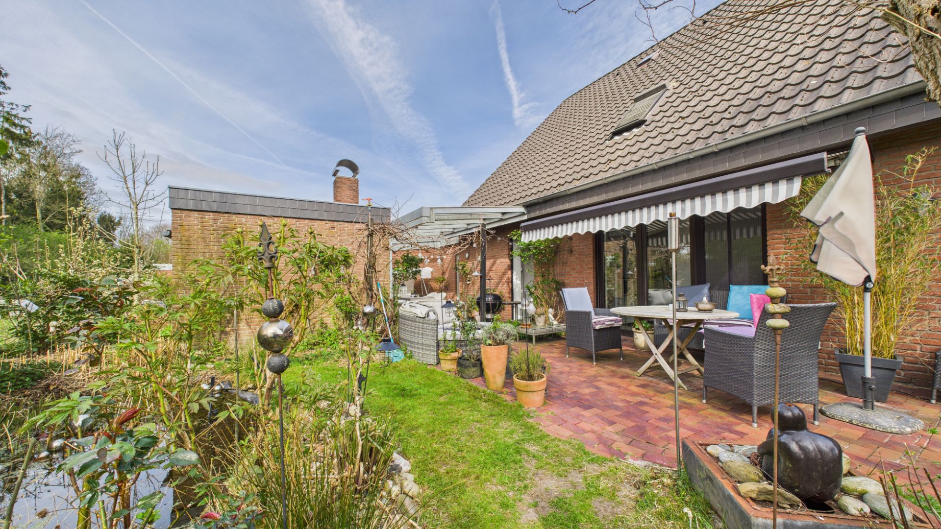 Terrasse mit Sitzmöbeln, Sonnenschutz und Pflanzen im Garten eines Wohnhauses.