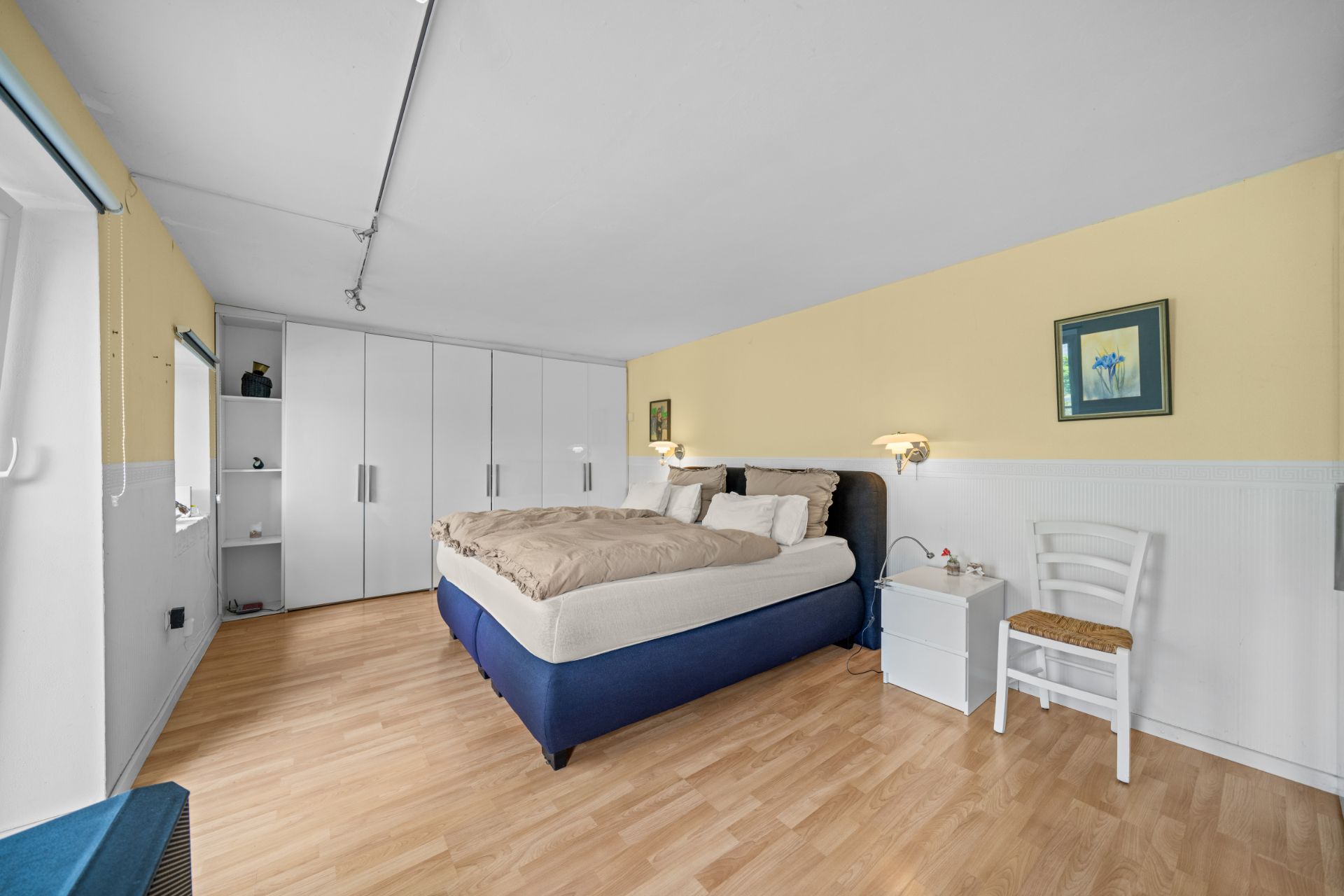 Schlafzimmer mit Doppelbett, Kleiderschränken, Nachttisch und Stuhl auf hellem Holzboden.