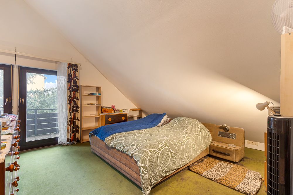 Schlafzimmer mit Doppelbett, grünem Teppich, Schreibtisch, Regal und Zugang zu einem Balkon.