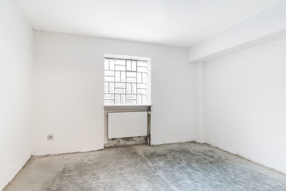 Leerer Raum mit weißen Wänden, einem Fenster und sichtbarem Heizkörper unter dem Fenster.