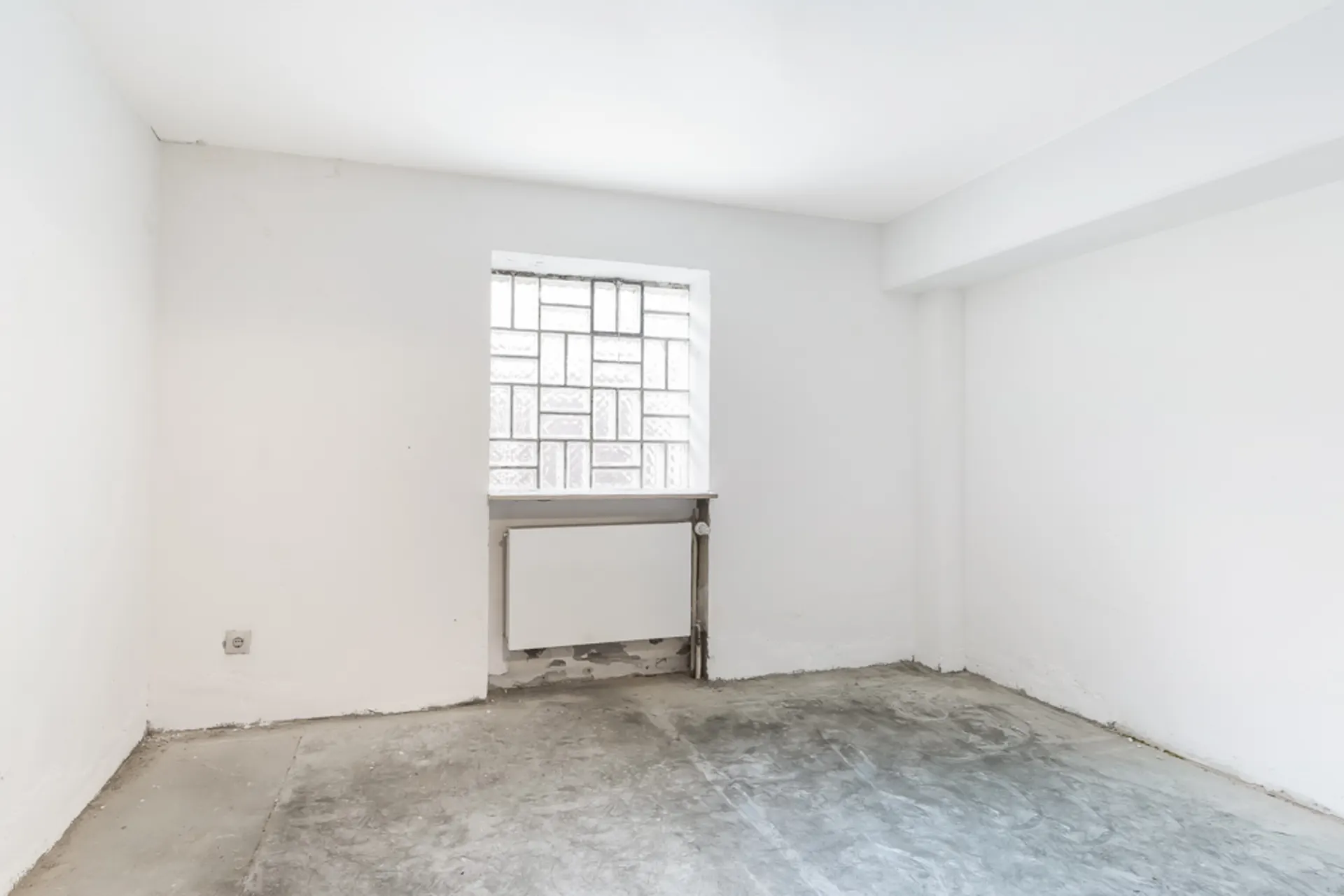 Leerer Raum mit weißen Wänden, einem Fenster und sichtbarem Heizkörper unter dem Fenster.