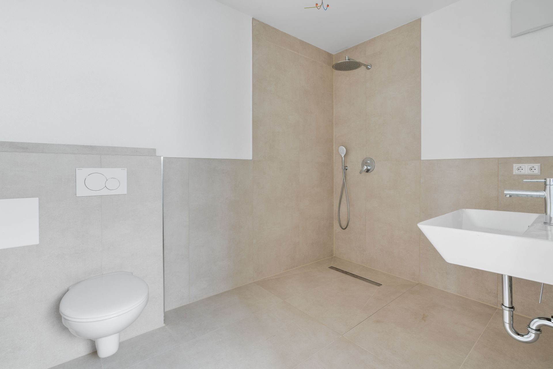 Modernes, barrierefreies Bad mit Dusche, Waschbecken und WC, beige Fliesen an Wand und Boden.
