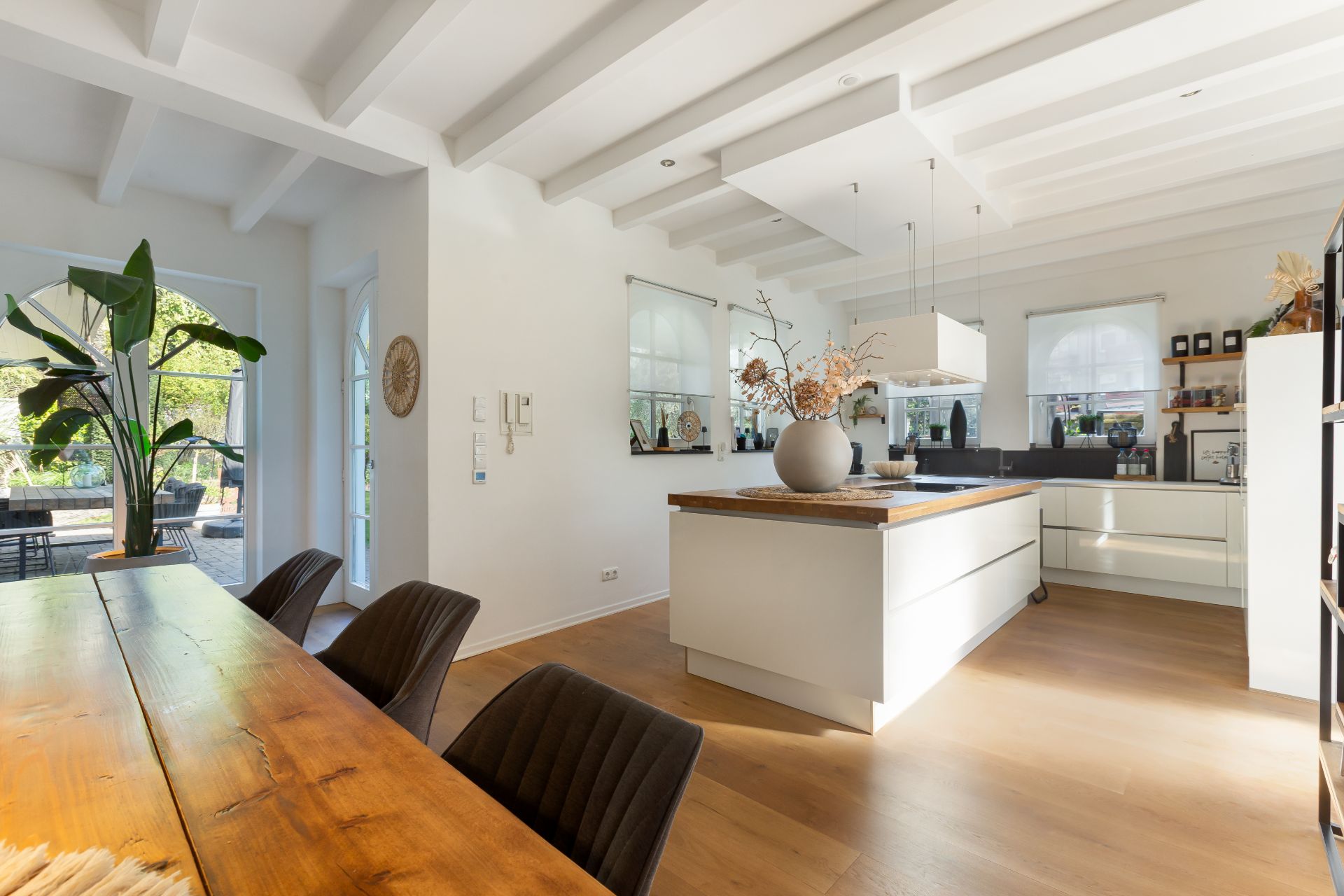 Moderne, helle Küche mit Kücheninsel, Esstisch und großen Fenstern mit Gartenblick.