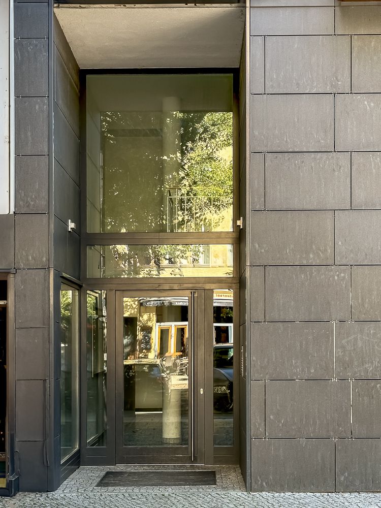 Glas-Eingangstür eines modernen Wohngebäudes mit dunkler Fassade.