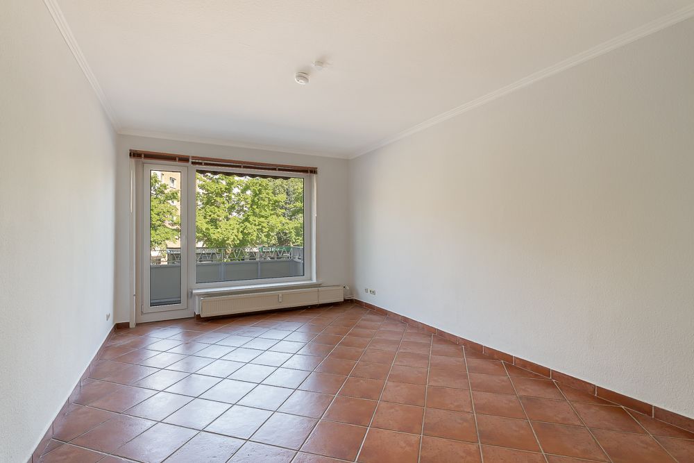 Leeres Zimmer mit Terrakottafliesen, großem Fenster und Zugang zu einem Balkon.