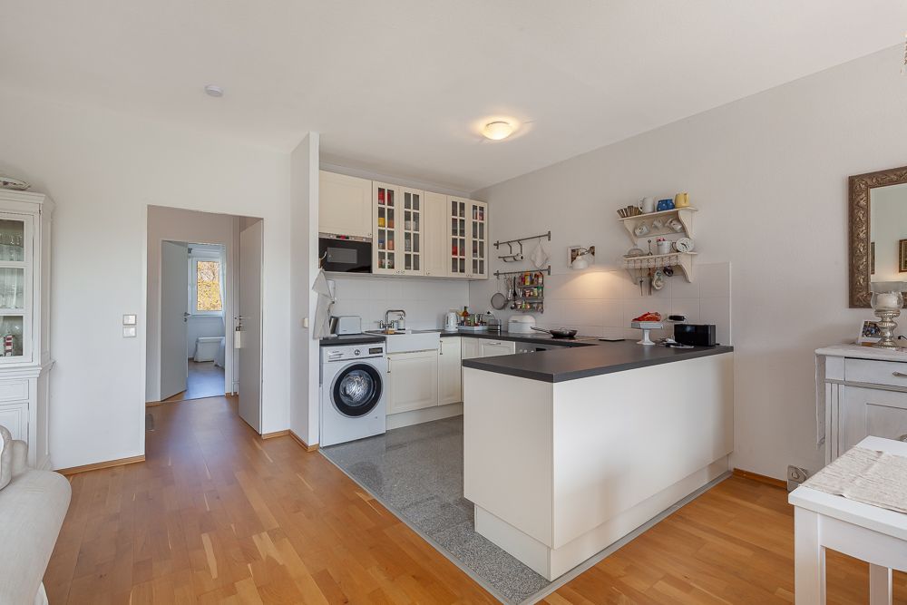 Helle Küche mit Kochinsel, Waschmaschine und Holzfußboden in einer Wohnung.