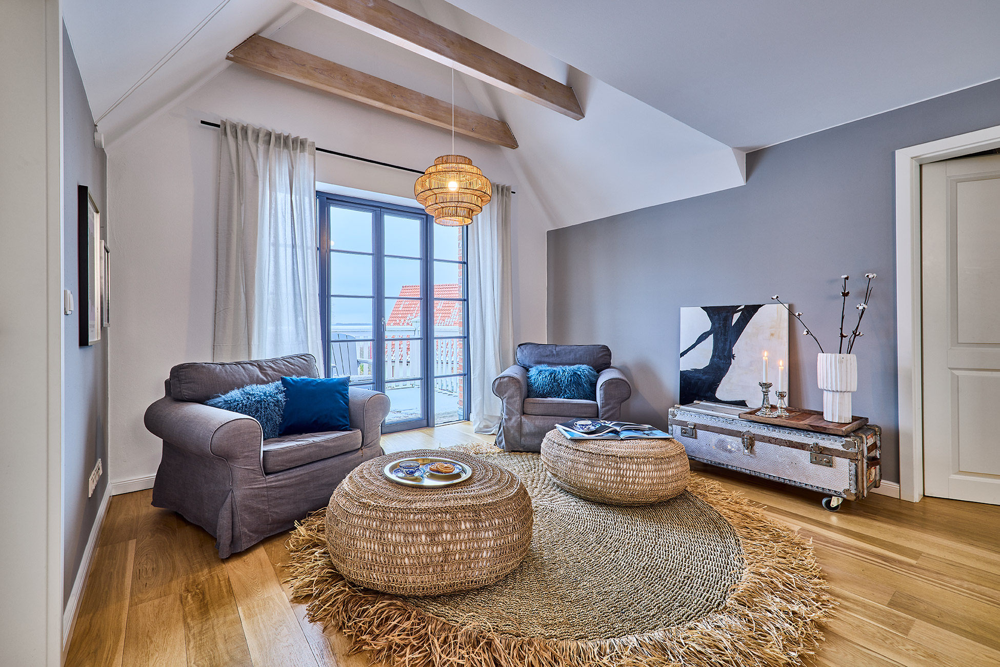 Helles Wohnzimmer mit zwei Sesseln, runder Teppich, niedrigen Tischen und großer Fensterfront.