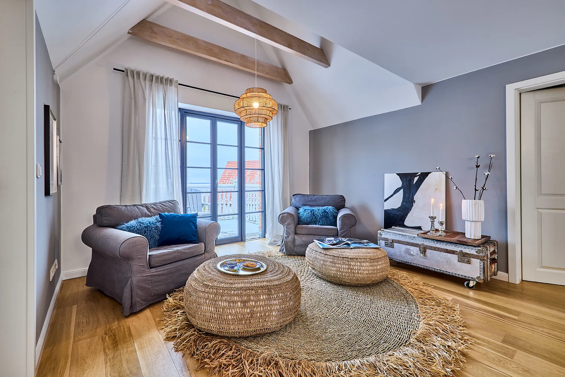 Helles Wohnzimmer mit zwei Sesseln, runder Teppich, niedrigen Tischen und großer Fensterfront.
