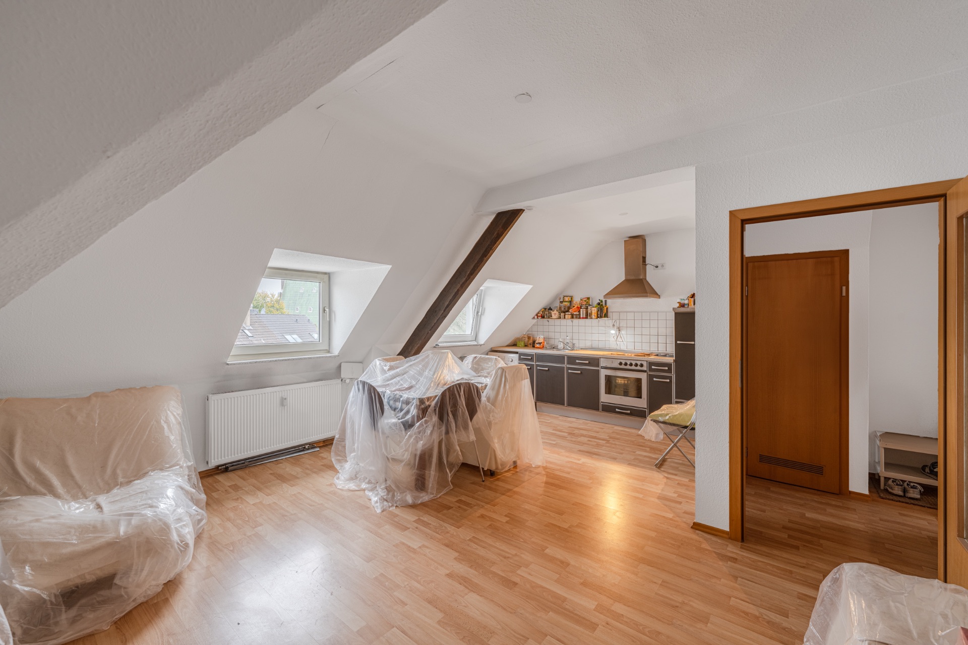 Wohnzimmer mit offener Küche, Dachschrägen, überzogenen Möbeln und Holzfußboden.