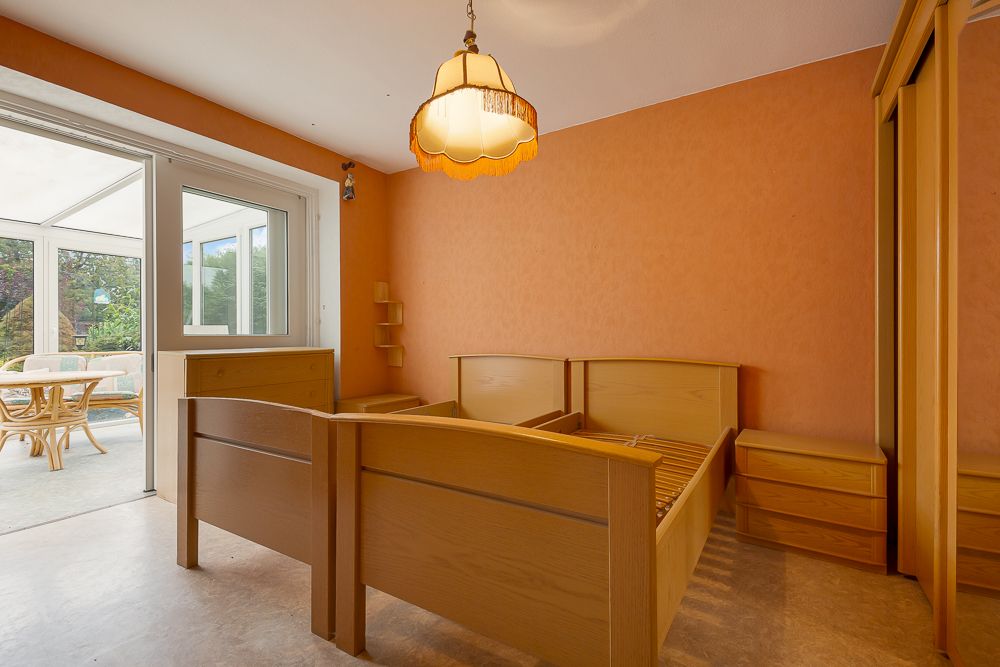 Zimmer mit zwei Holzbetten, Nachttischen, Kleiderschrank und Zugang zu einem Wintergarten.