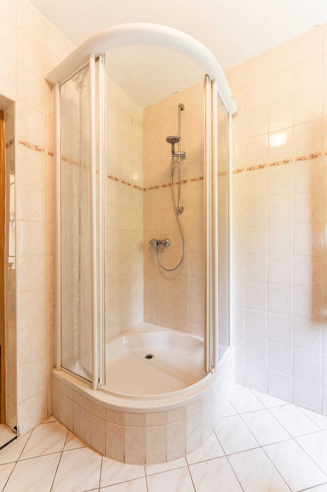 Eckeinstieg-Dusche mit Glaswänden und Handbrause in gefliestem Badezimmer.