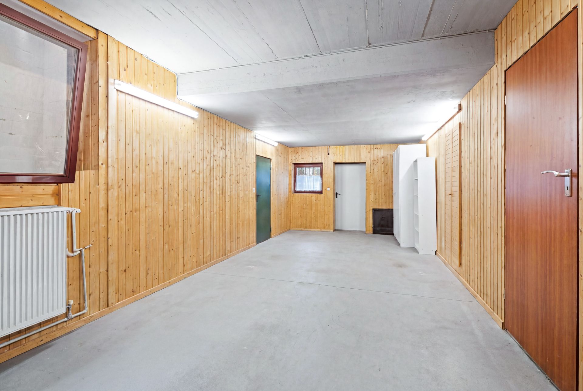 Heller Kellerraum mit Holzverkleidung, Betonboden, Heizkörper und mehreren Türen.