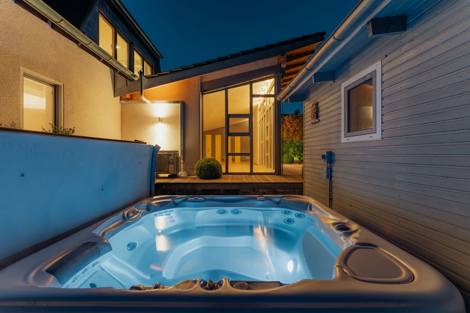 Beleuchteter Whirlpool im Innenhof eines modernen Wohnhauses bei Nacht.
