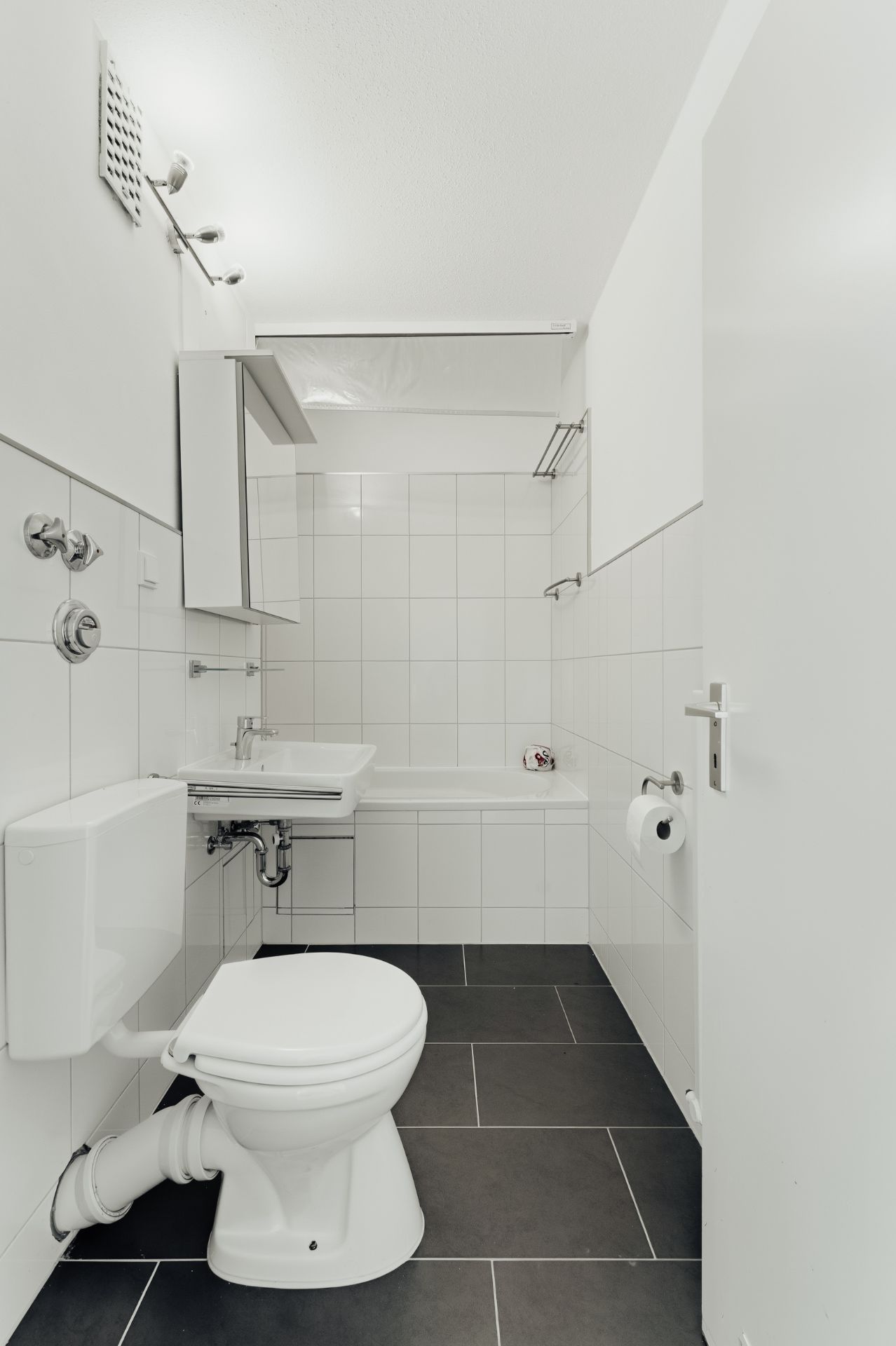 Modernes, weiß gefliestes Badezimmer mit Toilette, Waschbecken und Badewanne.