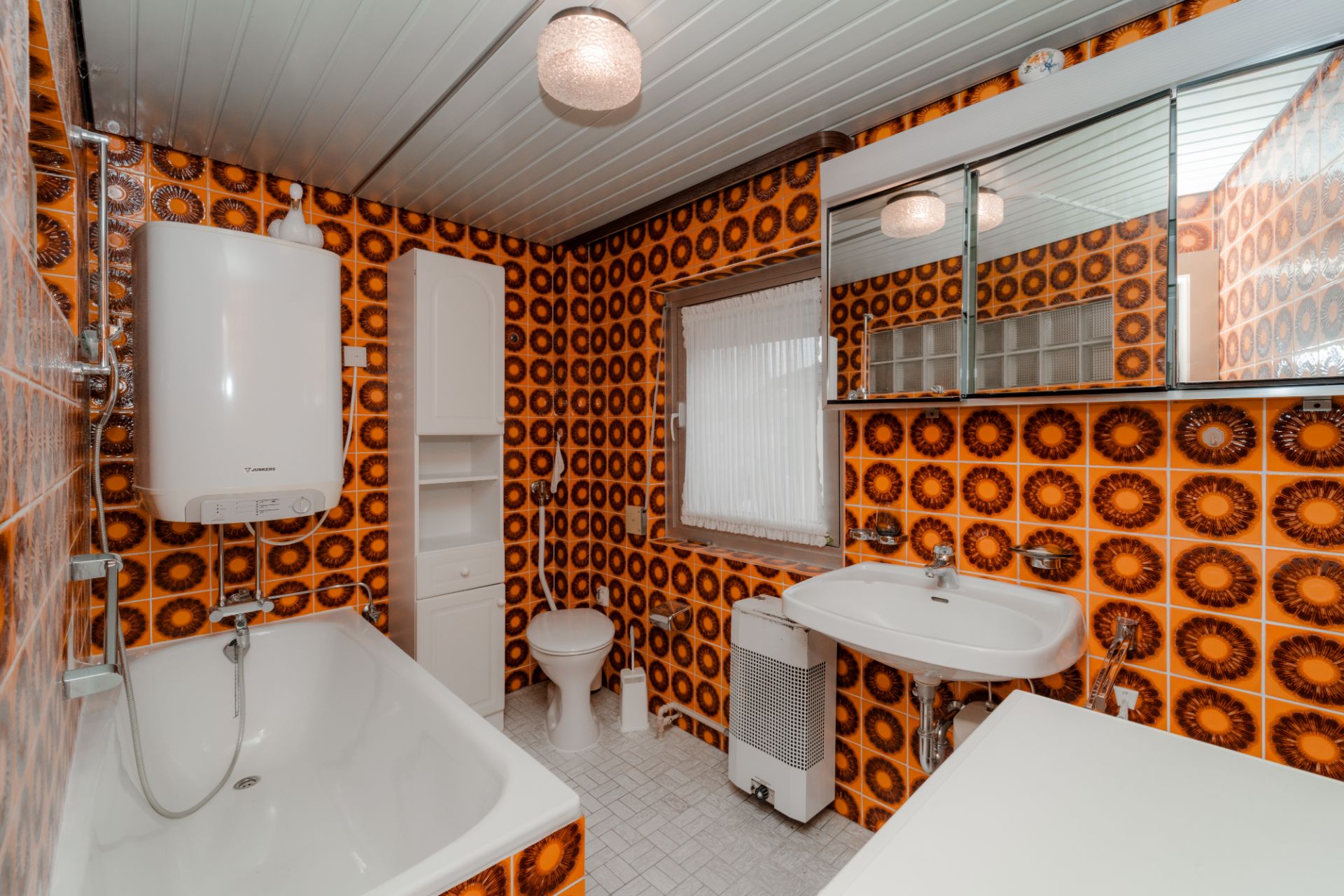 Badezimmer mit Badewanne, Waschbecken, Toilette und orange-braunen Fliesen mit Muster.