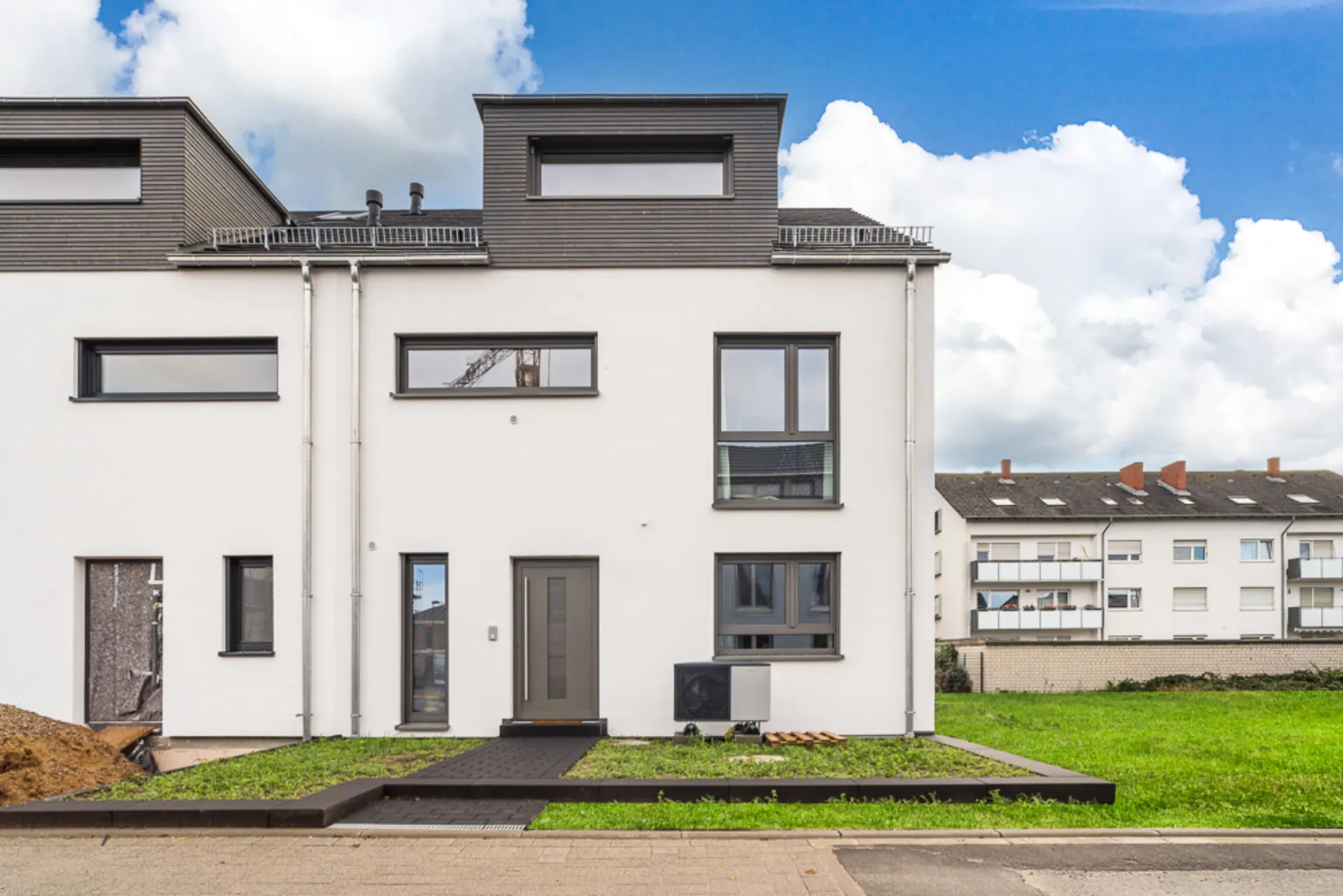 Moderne Doppelhaushälfte mit flachem Dach und großen Fenstern, davor Rasen und Gehweg.