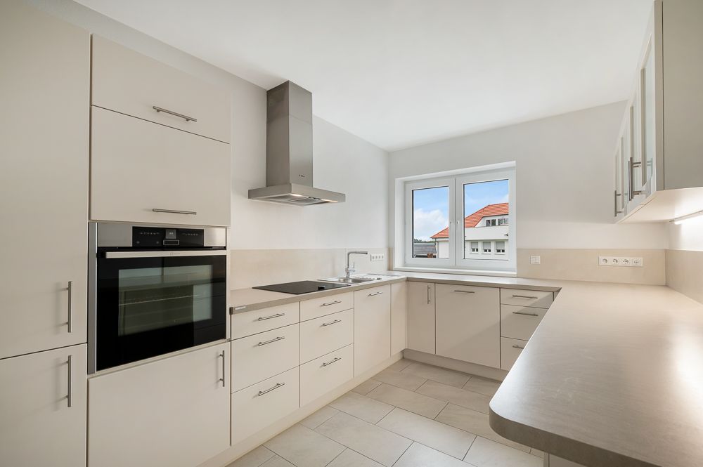 Moderne, helle Einbauküche mit Backofen, Herd, Dunstabzugshaube und Fenster.