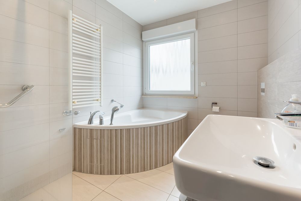 Modernes Badezimmer mit Eckbadewanne, großem Waschbecken und Fenster.