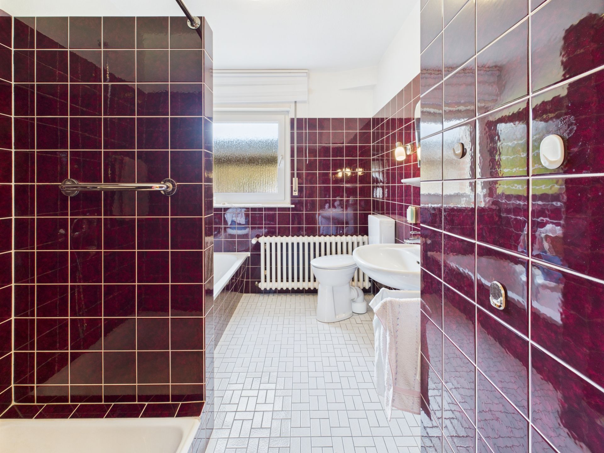 Badezimmer mit dunkellila Fliesen, weißem Waschbecken, Toilette und Fenster.