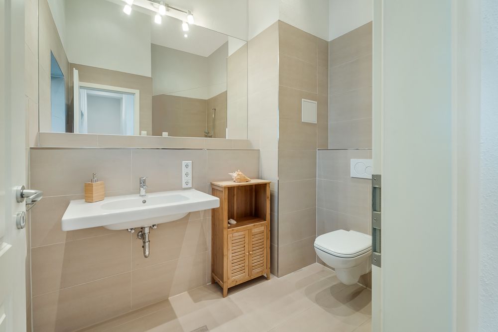 Modernes Badezimmer mit Wandwaschbecken, Holzregal, Spiegel und Hänge-WC.