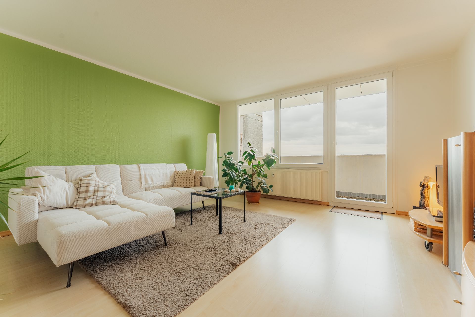 Helles Wohnzimmer mit weißem Sofa, grün gestrichener Wand und Zugang zum Balkon.