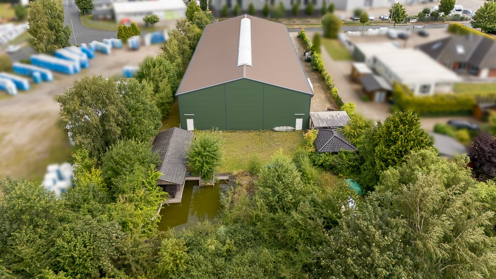 Luftaufnahme eines großen grünen Gebäudes mit Garten, Teich und Bäumen im Vordergrund.