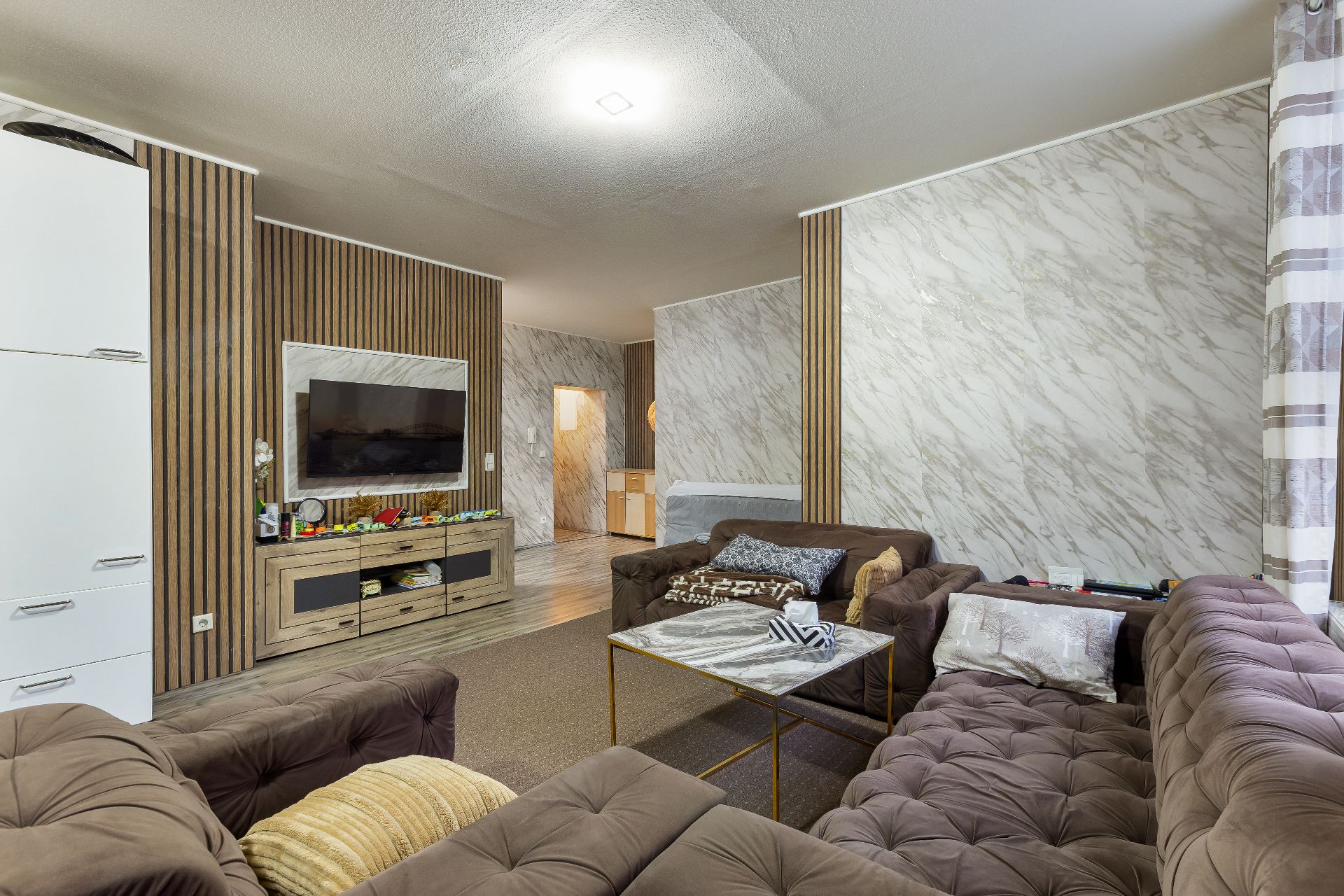 Wohnzimmer mit braunen Sofas, Wand-TV, Couchtisch und gemusterten Wänden.