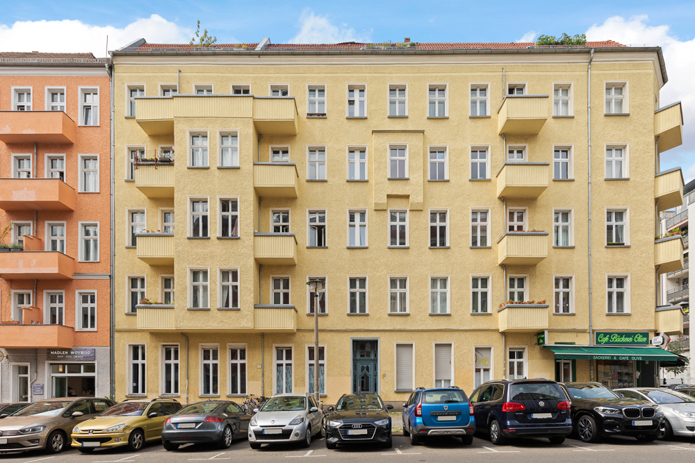 Mehrstöckiges gelbes Wohnhaus mit Balkonen und parkenden Autos davor.