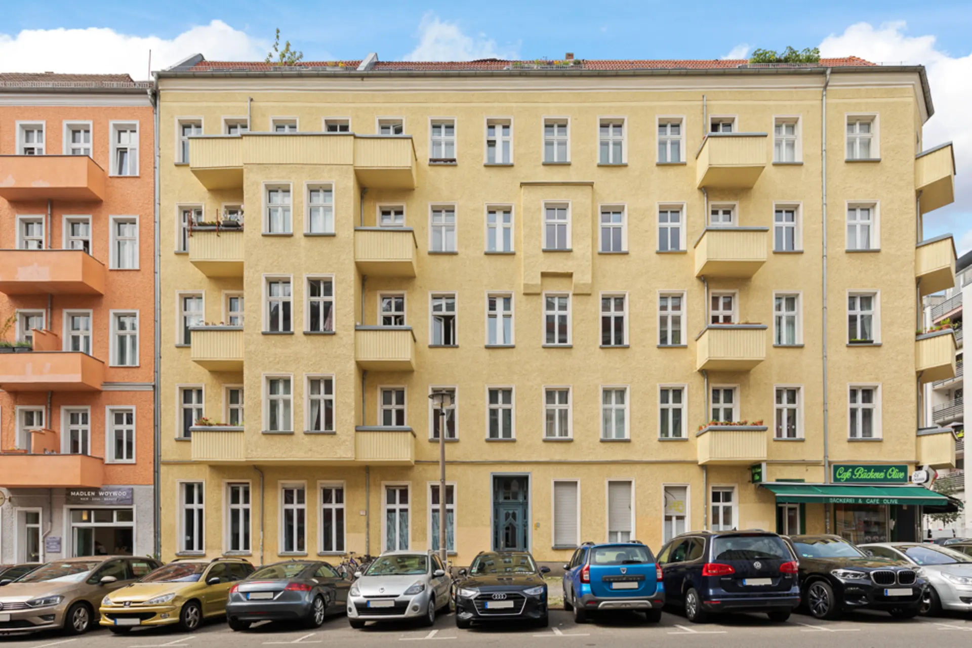 Mehrstöckiges gelbes Wohnhaus mit Balkonen und parkenden Autos davor.