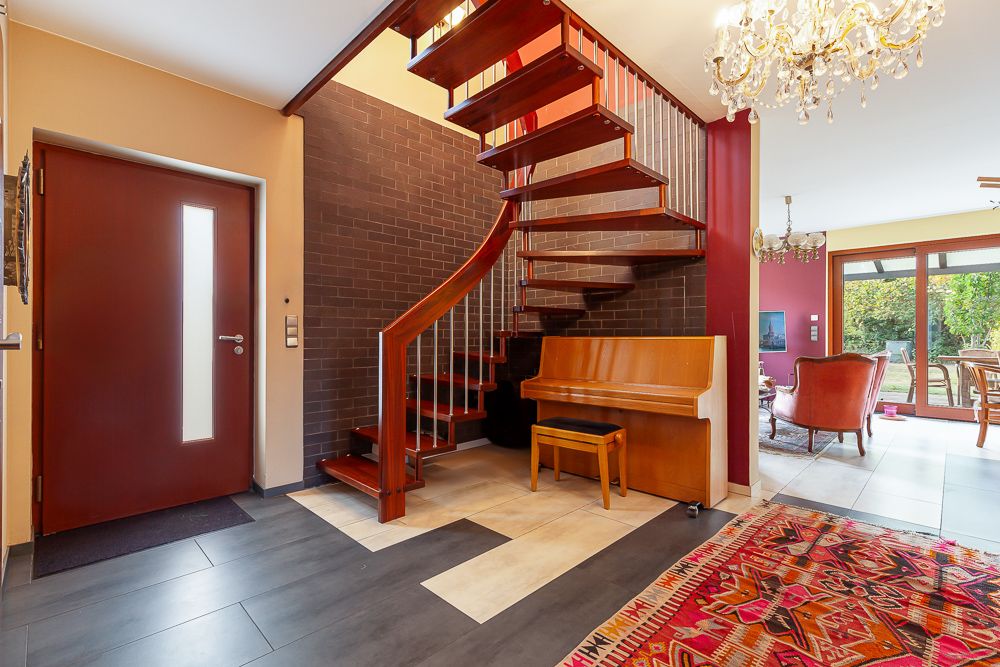Eingangsbereich mit moderner Treppe, Klavier, buntem Teppich und Blick ins Wohnzimmer mit Garten.