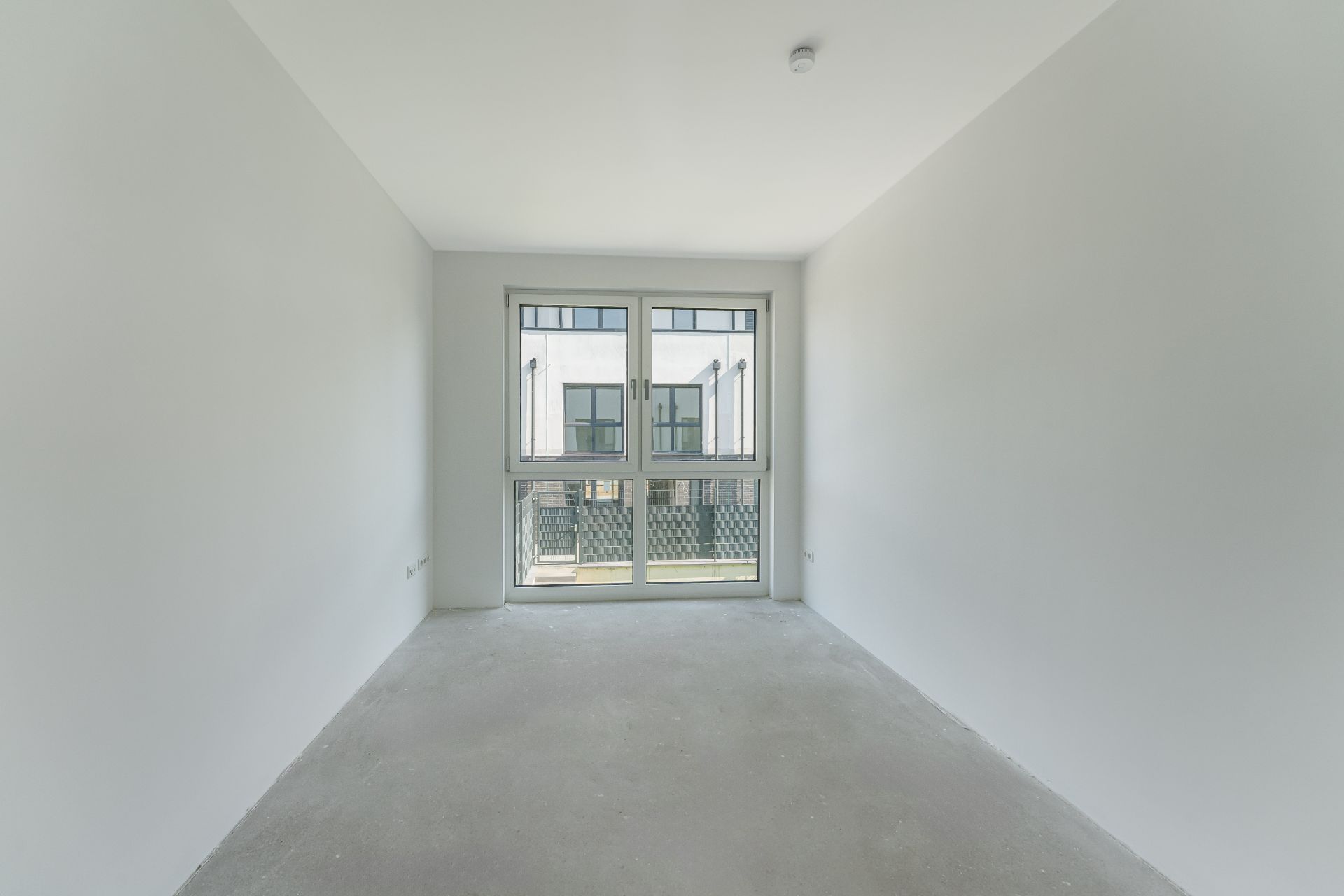 Leerer, heller Raum mit großem Fenster und grauem Boden.