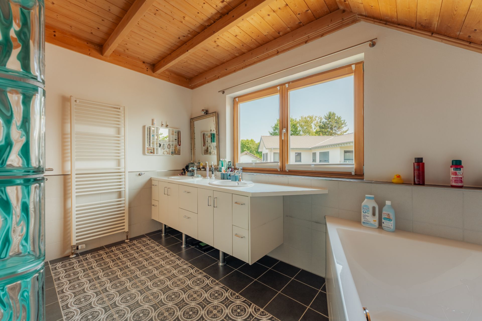 Helles Badezimmer mit Holzdecke, Badewanne, großem Fenster und Waschtisch mit Spiegel.