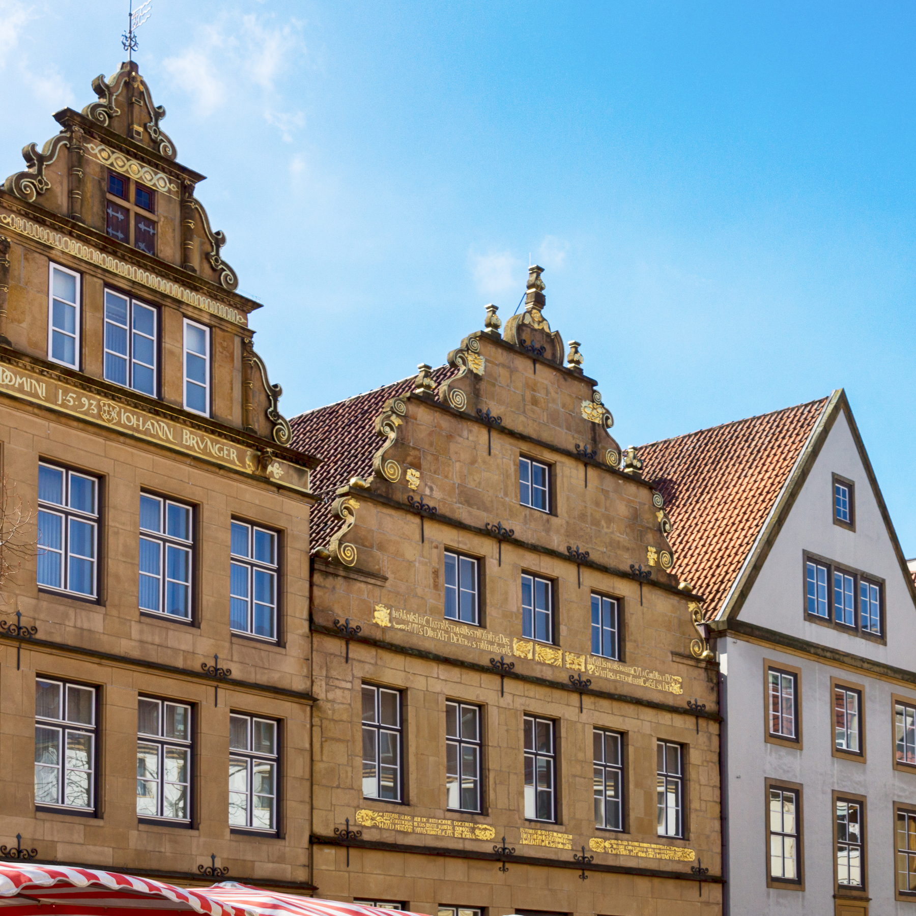 Historische Wohnhäuser mit verzierten Fassaden und roten Ziegeldächern bei blauem Himmel.
