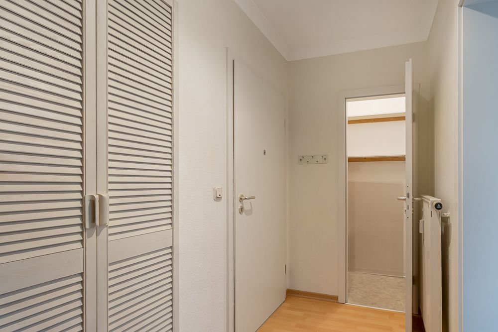 Heller Flur mit Holzlaminat, weißem Wandschrank und geöffneter Tür zu einem Abstellraum.