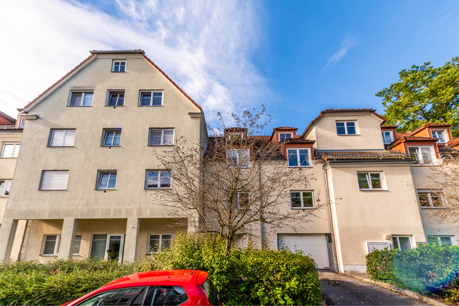 Mehrfamilienhaus mit hellen Fassaden, roten Dächern und einem roten Auto im Vordergrund.