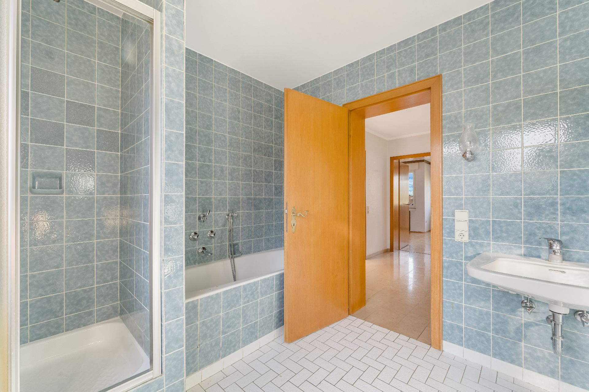 Badezimmer mit blauen Fliesen, Dusche, Badewanne, Waschbecken und geöffneter Holztür.