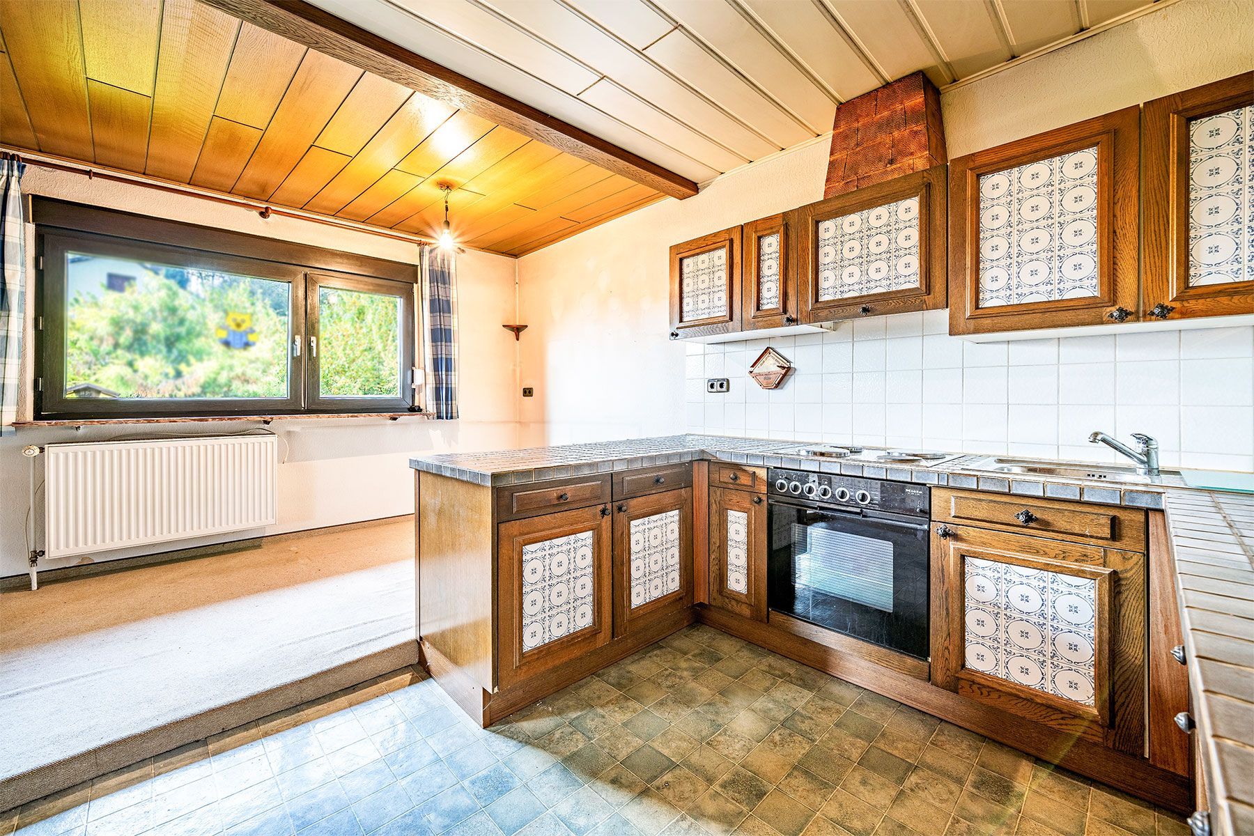 Küche mit Holzmöbeln, gemusterten Schranktüren und Fenster mit Blick ins Grüne.