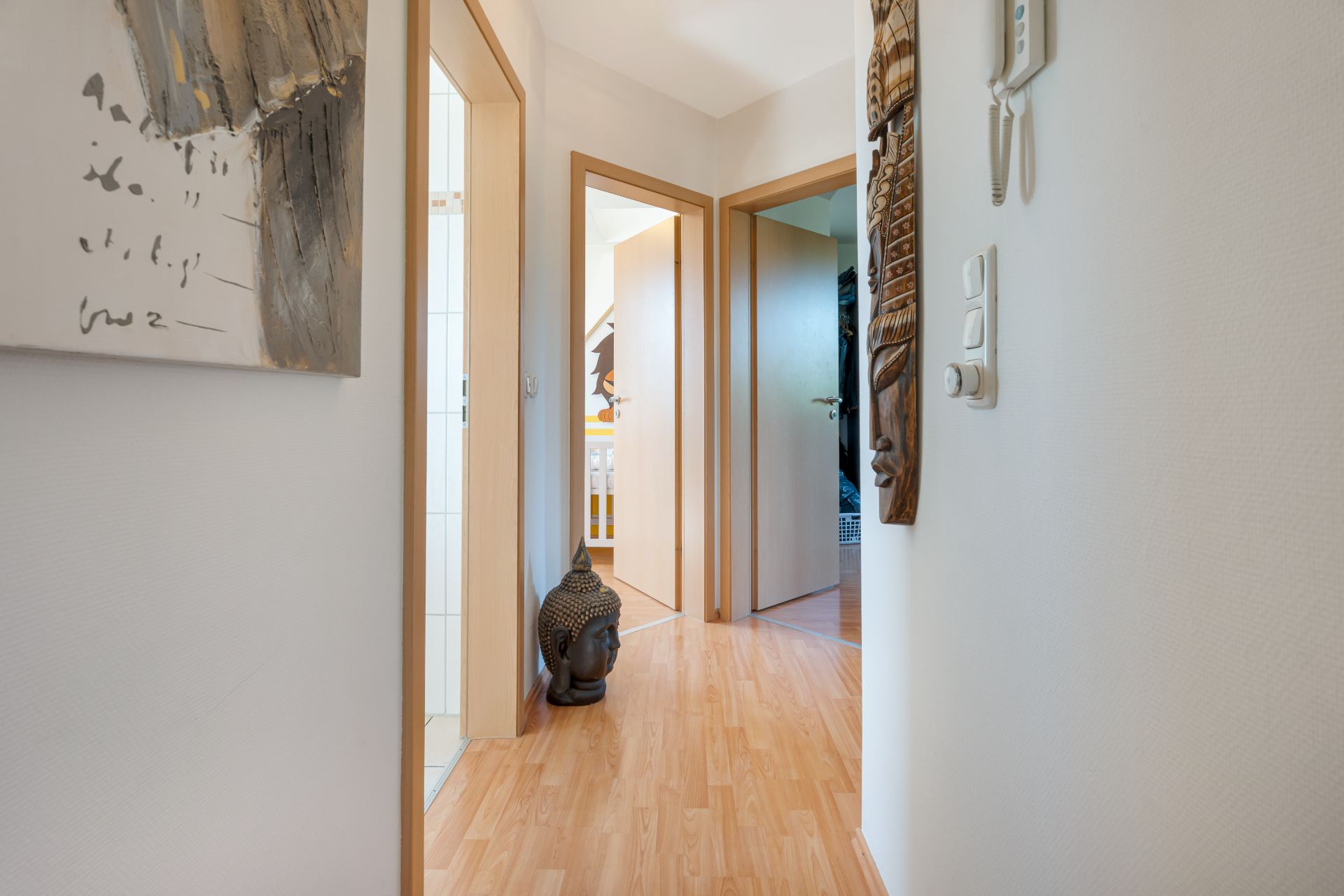Flur mit Holzfußboden, drei offenen Türen und einer Buddha-Kopf-Skulptur am Boden.